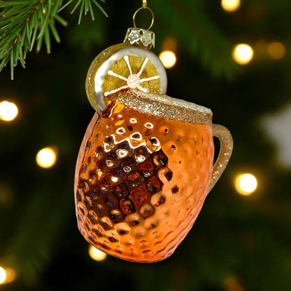 Decorative glass ornament shaped like a teacup with lemon slice on a Christmas tree.