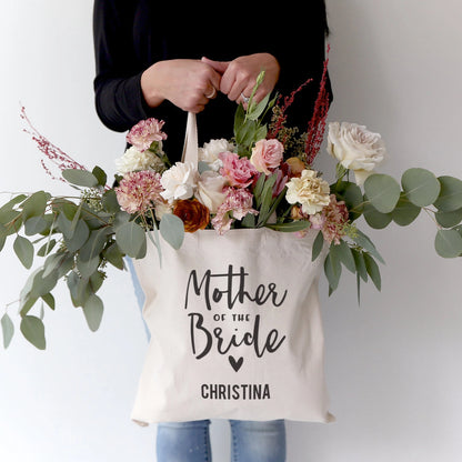 Person holding a tote bag labeled 'Mother of the Bride Christina' with flowers.