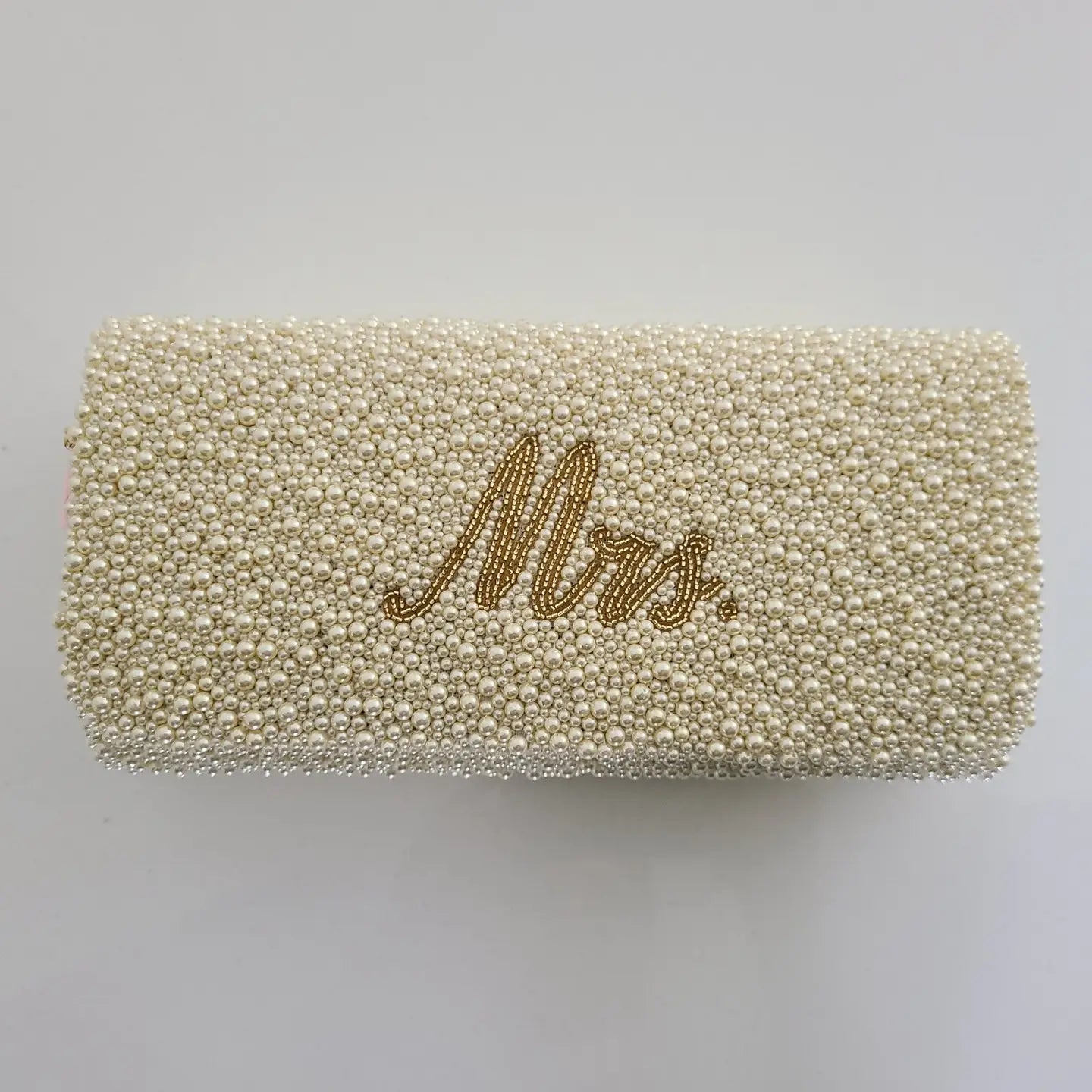 A rectangular clutch bag covered in small cream-colored beads with the word 'Mrs.' written in gold cursive script on the front, shown against a plain light gray background.