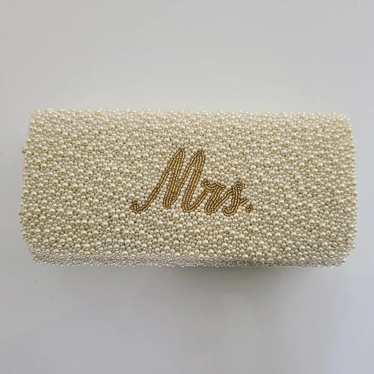 A rectangular clutch bag covered in small cream-colored beads with the word 'Mrs.' written in gold cursive script on the front, shown against a plain light gray background.