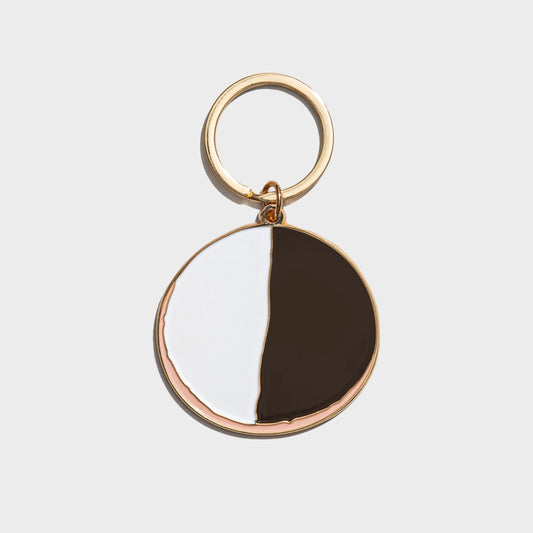 Keychain with gold ring and half-circle black and white design on a light gray background