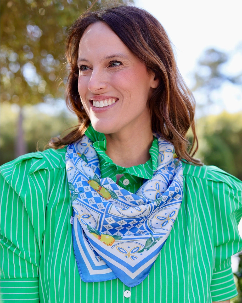 Woman wearing a blue patterned scarf over a green striped shirt with a blurred natural background