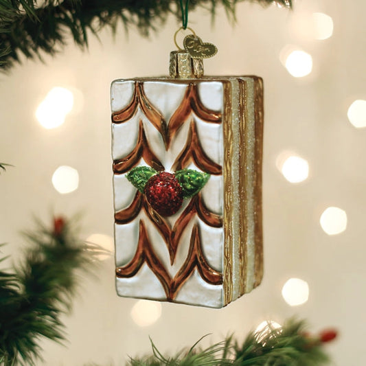 Decorative Christmas ornament with a book design and berries on a blurred Christmas tree background.