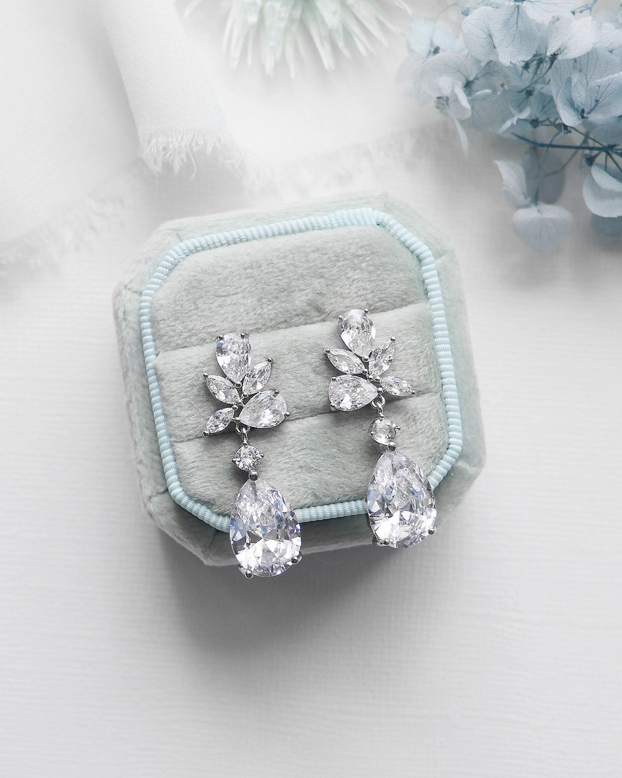 Pair of silver teardrop earrings on a light blue cushion with a soft white background