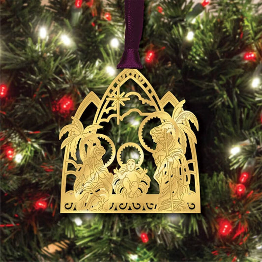 Gold nativity scene ornament hanging on a Christmas tree with purple ribbon.