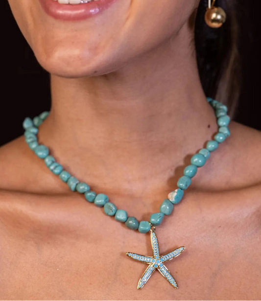 Woman wearing a turquoise beaded necklace with a starfish pendant on a dark background