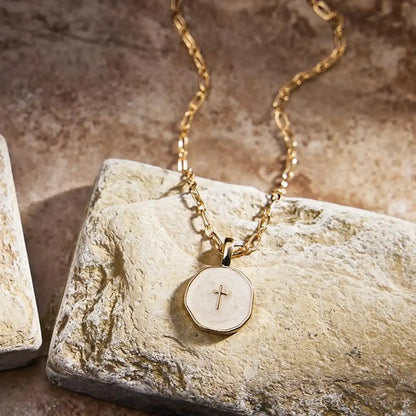 Gold necklace with a pendant featuring a cross on a stone surface