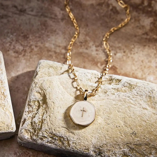 Gold necklace with a pendant featuring a cross on a stone surface