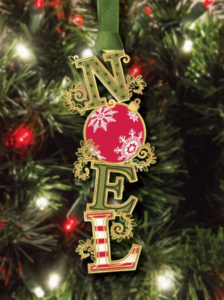 Decorative ornament spelling 'NOEL' with a pink ball and snowflake design, hanging on a Christmas tree.