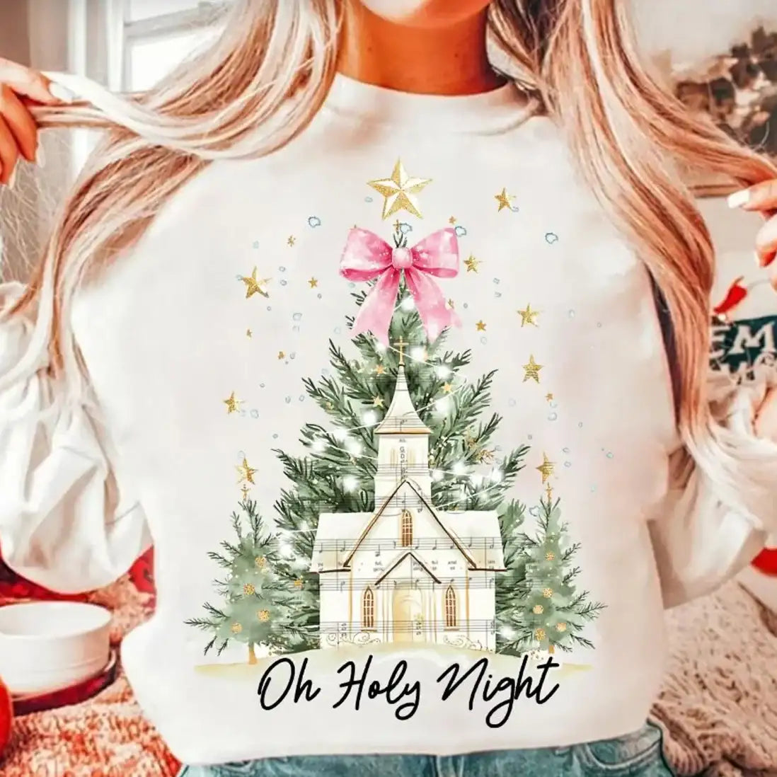 Person wearing a white sweatshirt with a Christmas-themed design featuring a church and trees, with 'Oh Holy Night' text.