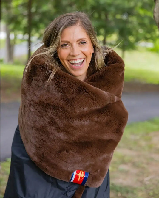 Woman wrapped in a brown blanket outdoors with trees in the background