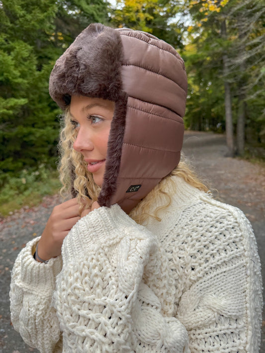 Person wearing a brown winter hat with fur trim outdoors