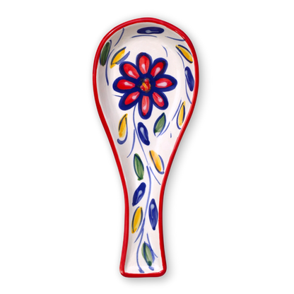 A white ceramic spoon rest decorated with a red and blue flower motif and blue, green, and yellow leaf accents, outlined with a red border, shown on a plain white background.