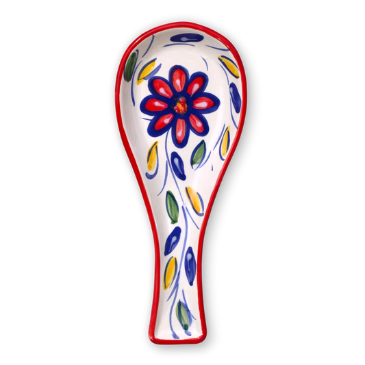 A white ceramic spoon rest decorated with a red and blue flower motif and blue, green, and yellow leaf accents, outlined with a red border, shown on a plain white background.