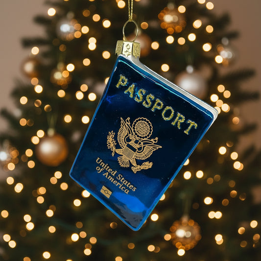 Decorative ornament shaped like a blue passport with gold text and design on a white background