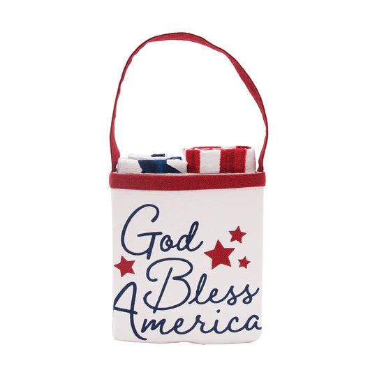 A white fabric tote bag with a red handle, featuring the text 'God Bless America' in navy blue script with red stars on the front. The bag is shown containing folded items, photographed against a solid white background.