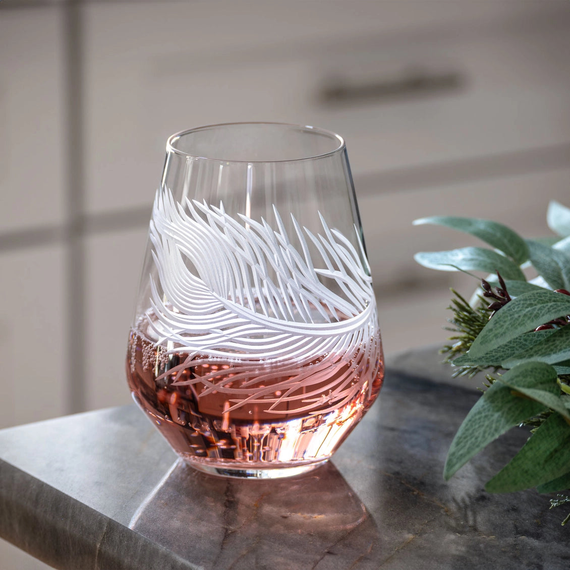 Glass with feather design filled with pink liquid on a marble surface