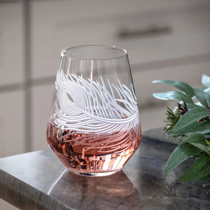 Glass with feather design filled with pink liquid on a marble surface