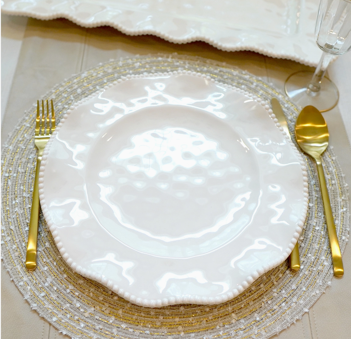 Perlette cream melamine dinner plate with beaded ruffled rim styled with gold flatware and decorative charger
