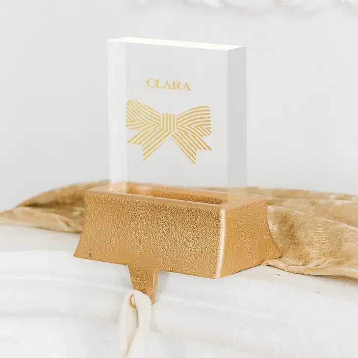 White box with gold bow design and 'Clara' branding on a beige stand against a white background