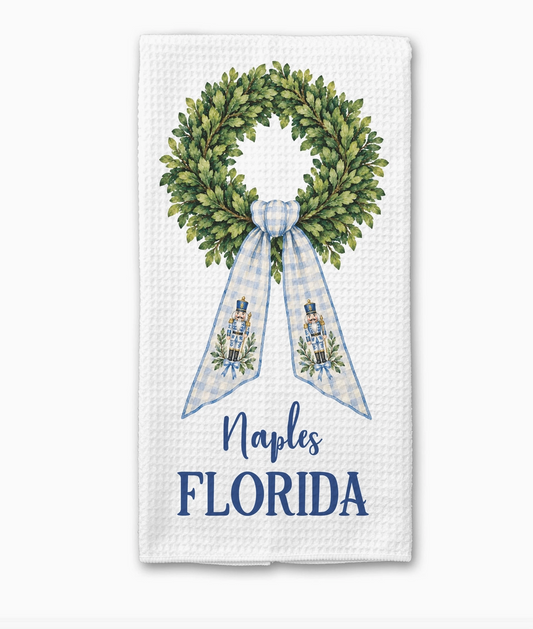 Personalized chinoiserie nutcracker Christmas kitchen towel featuring a boxwood wreath, blue gingham ribbon and custom Naples Florida text.
