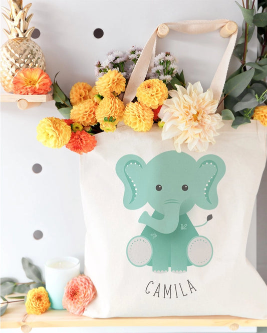 Tote bag with a green elephant design and 'Camila' text, surrounded by flowers and decorative items.