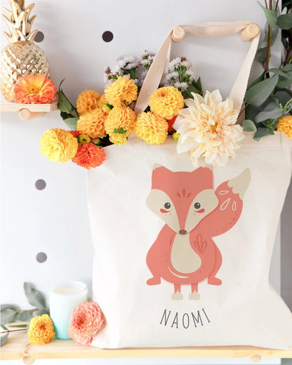 White tote bag with a fox design and 'Naomi' text, surrounded by flowers and decorative items.