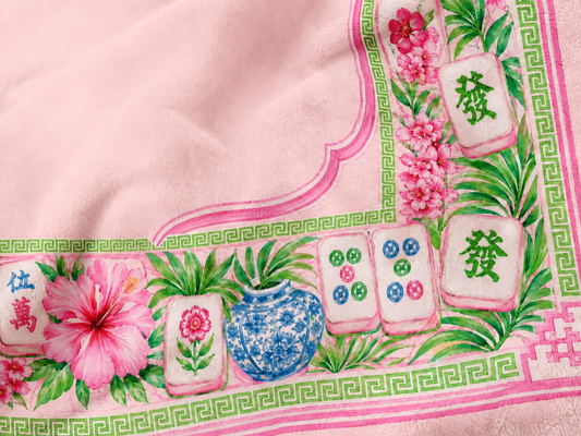 Close-up of pink personalized Mahjong blanket with hibiscus flowers, tropical greenery, blue and white vase and colorful Mahjong tiles.