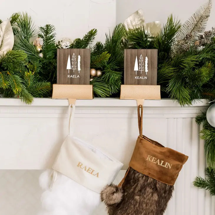 Two wooden name signs on a mantel with Christmas stockings below.