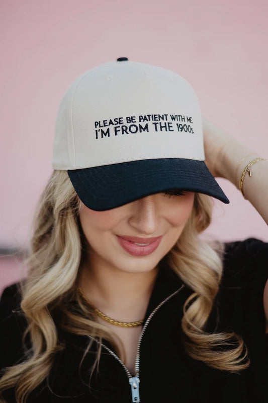 Woman wearing a cap with text that says please be patient with me im from the 1900's against a pink background