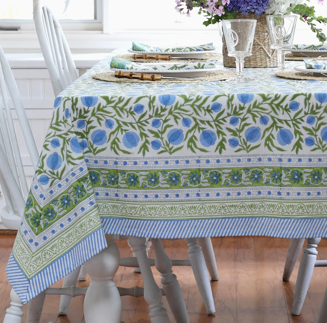 Dining table set with a floral patterned tablecloth in a bright room.