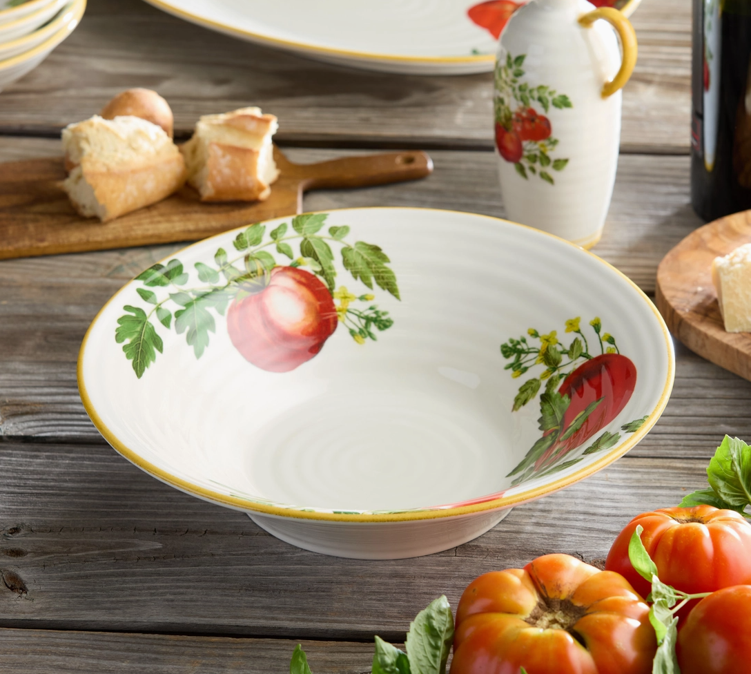 Decorative ceramic bowl with tomato design on a wooden table with bread and a mug.