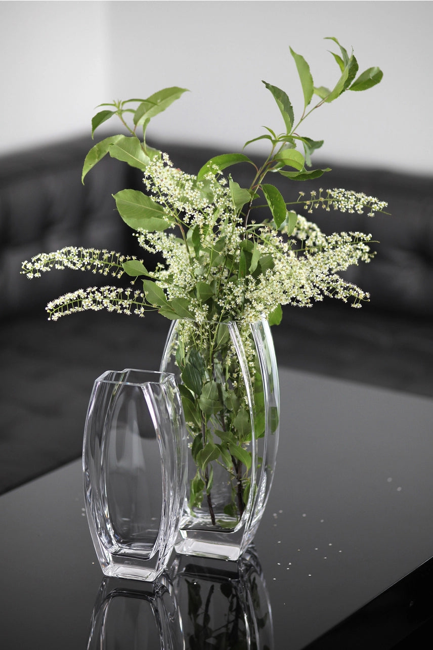 Two clear glass vases with greenery on a reflective surface