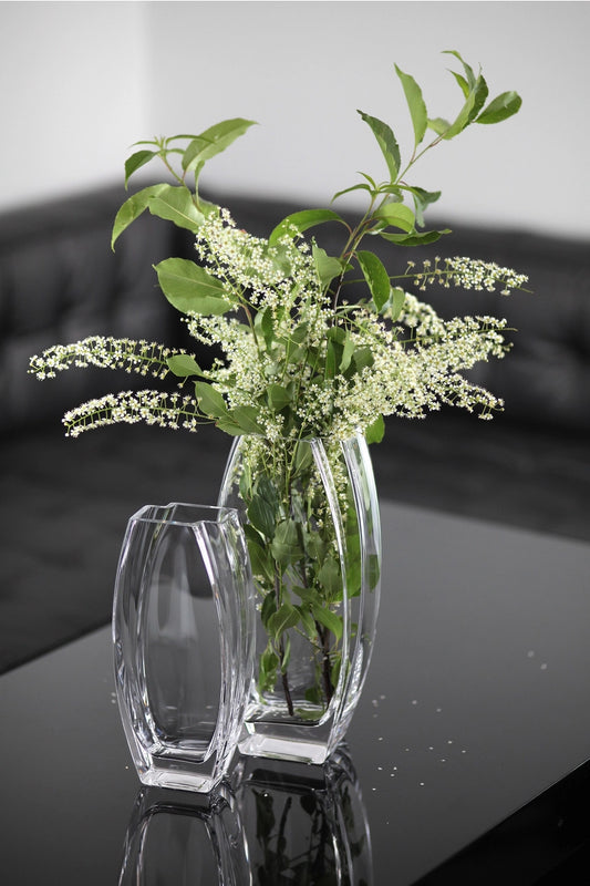 Two clear glass vases with greenery on a reflective surface