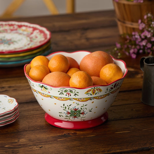 Decorative ceramic bowl with floral patterns filled with oranges on a wooden table.