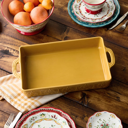 Yellow rectangular baking dish on a wooden table with decorative plates and oranges.