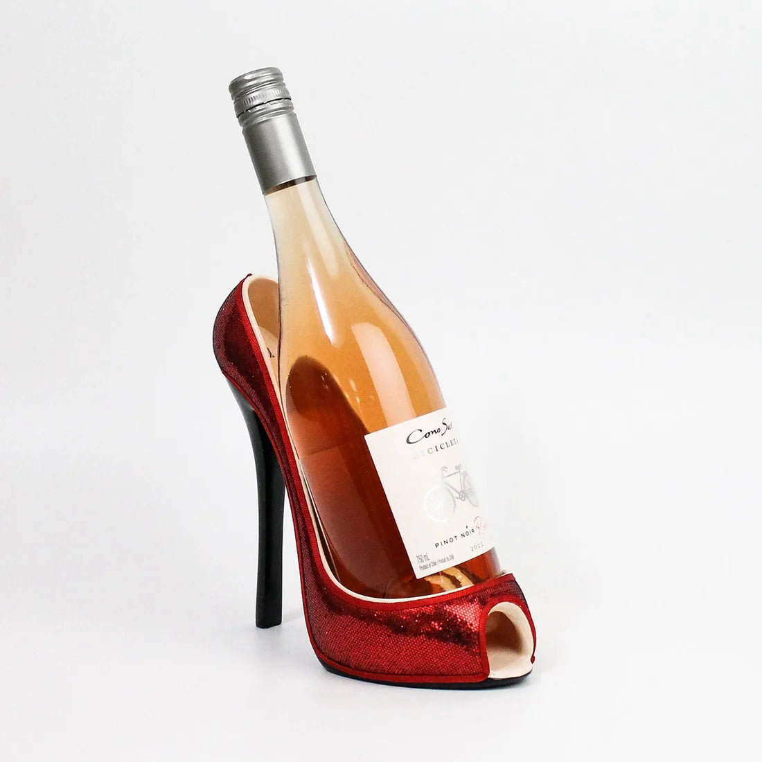A novelty wine bottle shaped like a red glitter high-heeled shoe, filled with rosé ginese wine, photographed on a clean white background.