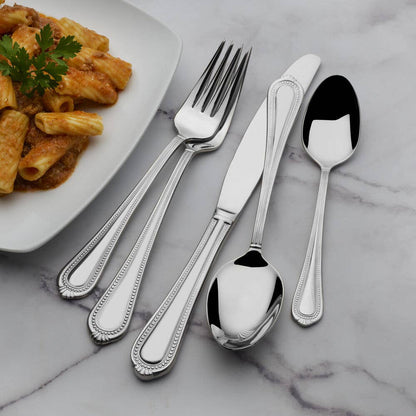 Silver cutlery set on a marble surface with a plate of pasta.