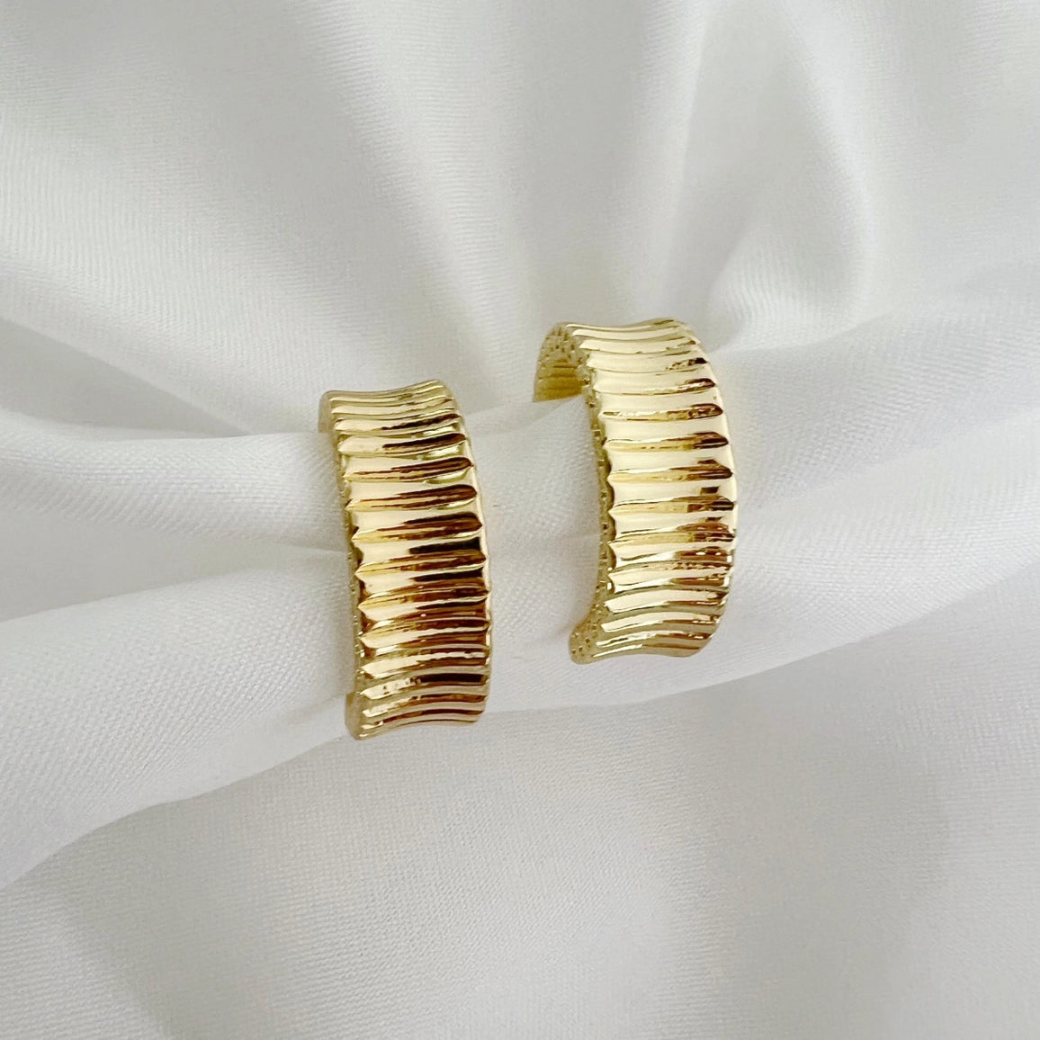 Gold hoop earrings on a white fabric background