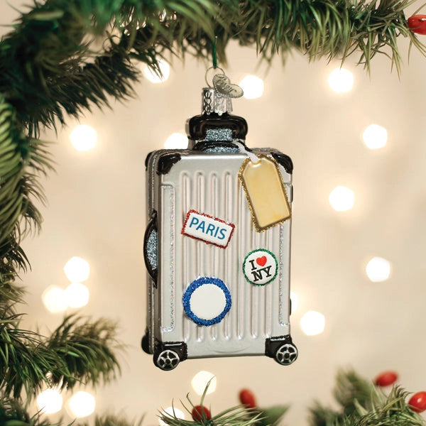 Christmas ornament shaped like a suitcase with 'Paris' and 'I ❤️ NY' tags, hanging on a decorated tree.