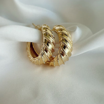 Gold hoop earrings on a white fabric background