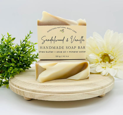 Handmade soap bar with packaging on a wooden stand, surrounded by flowers and greenery.
