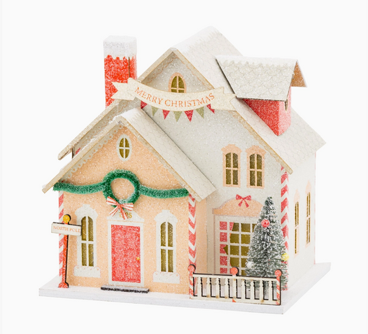 Santa’s House lighted Christmas village decoration with snowy glittered roof, Merry Christmas banner, wreath, red door and miniature Christmas tree.