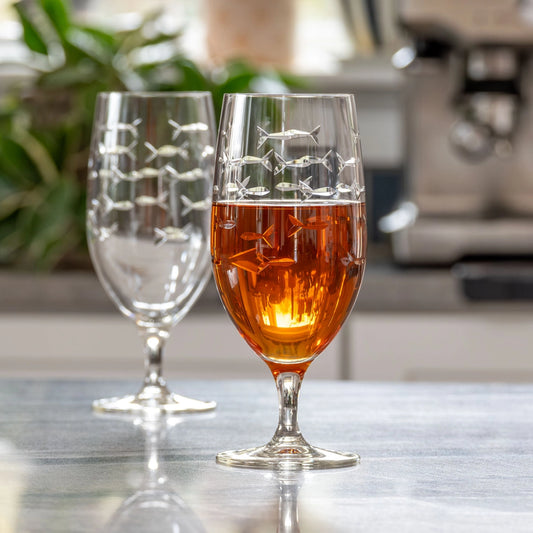 Two wine glasses with engravings on a table, one filled with amber liquid.
