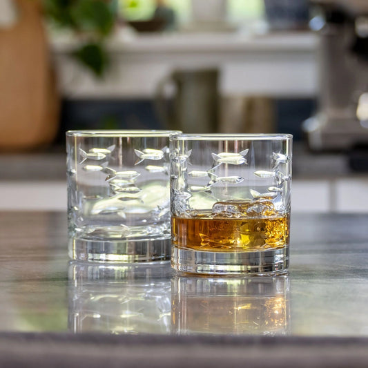 Two glasses of whiskey on a reflective surface with a blurred indoor background