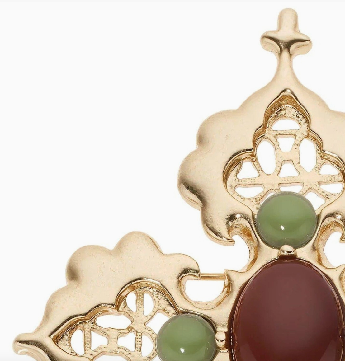 Close-up of Olivia Riegel gold cross brooch with green and reddish-brown cabochon accents