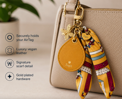 Mustard yellow AirTag holder with patterned scarf and gold-plated charms attached to a beige handbag