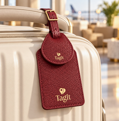 Burgundy textured luggage tag with gold-tone details attached to a cream suitcase handle.