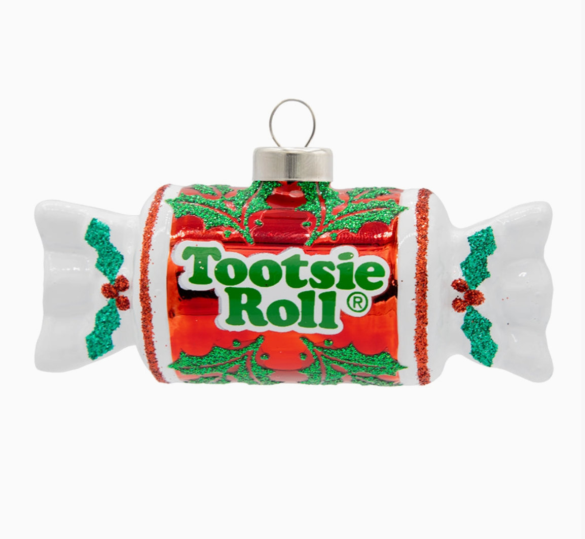 A Tootsie Roll Christmas ornament shaped like a candy wrapper, featuring a red and green holiday label with holly motifs and the Tootsie Roll logo, on a plain white background.