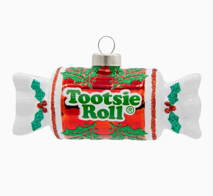 A Tootsie Roll Christmas ornament shaped like a candy wrapper, featuring a red and green holiday label with holly motifs and the Tootsie Roll logo, on a plain white background.
